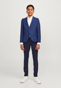 Blazer blu scuro con due bottoni, due tasche anteriori e camicia bianca sotto. Abbinato a pantaloni blu scuro e sneaker bianche.