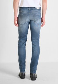 Vaqueros ajustados de denim azul, con un lavado desgastado, cinco bolsillos y una cintura de altura media, combinados con zapatos negros.