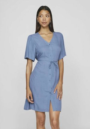 Robe bleu clair avec des manches courtes à volant, décolleté en V et devant à boutons. Présente une taille à nouer et une fente au niveau de l'ourlet. Texture de tissu lisse.