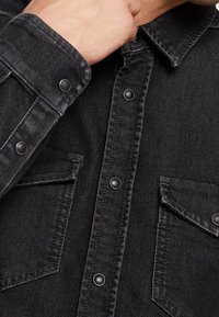 Zwarte spijkerblouse met drukknoopjes, puntige kraag en twee opgestikte zakken. Kenmerkt zich door de gestructureerde stof en een slank ontwerp.