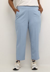 Pantalones ajustados de color azul claro con corte recto, bolsillos laterales y textura suave, combinados con zapatillas blancas y marinas.