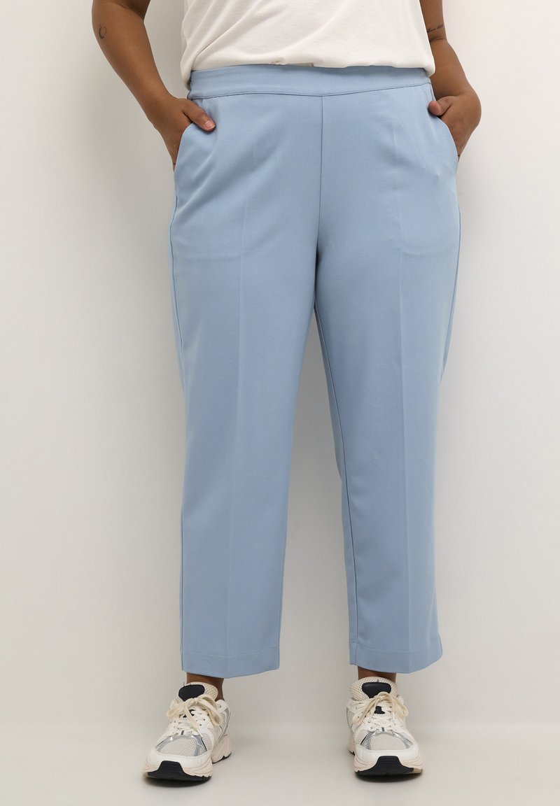 Pantalones ajustados de color azul claro con corte recto, bolsillos laterales y textura suave, combinados con zapatillas blancas y marinas.