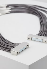 Collier en corde tressée grise avec deux accents rectangulaires en métal argenté dotés d'un incrustation de panneau bleu clair, fixé par des vis à chaque extrémité.