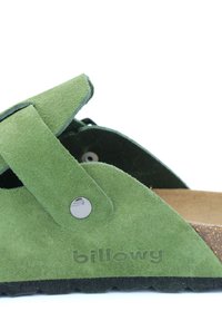 Sandale en suède verte avec une semelle en liège, sangle ajustable avec un bouton-pression métallique et semelle en caoutchouc texturée. Nom de la marque "billowy" embossé sur le côté.