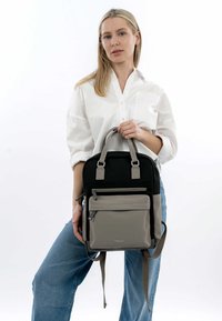Mochila gris y negra hecha de tela duradera, con asas acolchadas, un bolsillo frontal con cremallera y correas ajustables.