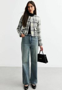 Veste croppée à carreaux noir et blanc, jean bleu taille haute, ballerines noires à bout rond, et sac à main noir. Tissu lisse et structuré avec une coupe ample.