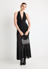 Rochie neagră cu guler halter, cu detalii strânse și suprapunere transparentă, asortată cu o geantă mică sclipitoare și cizme negre până la genunchi.