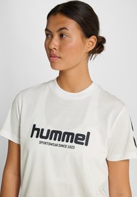 Hvid bomulds t-shirt med et sort "hummel" logo og teksten "SPORTSWEAR SINCE 1923," med korte ærmer og rund halsudskæring.
