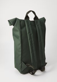 Sac à dos vert foncé en tissu résistant. Comprend un haut roulé, des poignées réglables et une base renforcée. Design minimaliste sans motifs.