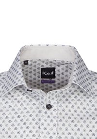 Camicia bianca con bottoni e un piccolo motivo floreale blu, colletto bianco a contrasto. Presenta una vestibilità regolare e un bottone nero sul davanti.