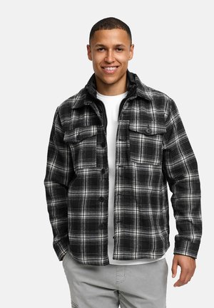 Svart- og hvitmønstret flanelljakke med to brystlommer, knapplukking og en myk tekstur, båret over en hvit crew neck T-skjorte.