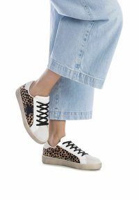 Sneakers with white and black materials, featuring a leopard print side panel and black laces. Rubber sole and low-profile design.