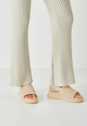 Sandali beige open-toe con tomaia in morbido suede e suola platform leggera; indossati con pantaloni in tessuto a coste chiaro.