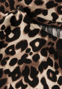 Kangas kuviolla, jossa on mustia pilkkuja vaaleanruskealla taustalla, pehmeällä tekstuurilla ja hieman roikkuvalla muotoilulla.