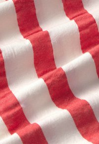 Cotton fabric featuring alternating wavy stripes in coral and white, with a soft texture and slight sheen, creating visual depth.