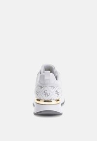 Zapatilla deportiva blanca con acentos dorados, patrón texturizado en los laterales, punta redondeada y suela gris contrastante. Con cuello acolchado y tira de agarre.
