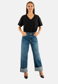Top a V in polka dot neri abbinato a pantaloni larghi a vita alta in denim blu, con orli risvoltati e tacchi alti neri.