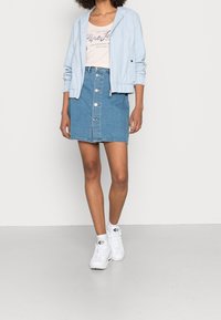 Světle modrá bomber bunda, béžové tričko s grafikou, džínsová minisukně s předními knoflíky a bílé tenisky s černými akcenty.