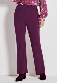 Lila weite Hosen aus weichem Stoff mit einem hohen elastischen Bund und Details an der Vordernaht. Kombiniert mit burgunderfarbenen Schuhen.