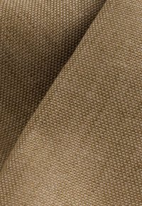 Närbild av tätt vävt beige tyg med ett texturerat, rutmönstrat mönster och en vikt sektion som lyfter fram materialets tjocklek.