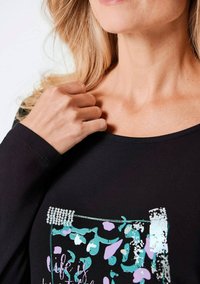 Schwarzes Langarmshirt mit Rundhalsausschnitt, das ein farbiges Grafikdesign und Strassakzente im Bereich der Brusttasche aufweist.