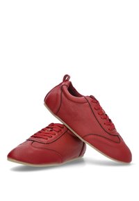 Zapatillas de cuero rojo con un acabado texturizado, punta redondeada y cuatro pares de ojales. Cuenta con una lengüeta trasera y costuras negras en contraste.
