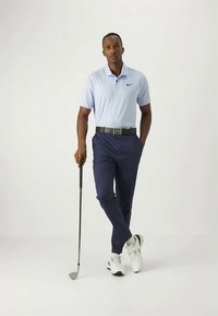 Outfit da golf maschile composto da una polo azzurra chiara con logo Nike, pantaloni blu scuro, scarpe bianche e un bastone da golf in mano.
