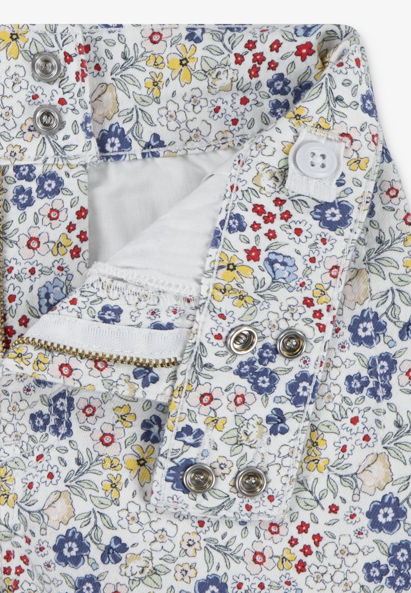 Tissu à motif floral en blanc, avec de petites fleurs rouges, bleues et jaunes. Comprend une fermeture à pression métallique et des détails de poche zippée.