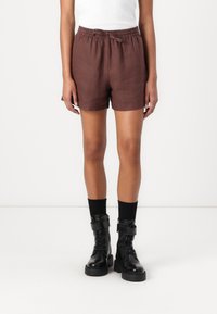 Shorts en lin marron avec une taille élastique et un cordon de serrage. Associés à des bottes noires à lacets et des chaussettes noires montantes.
