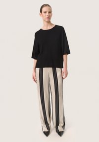 Black short-sleeve top paired with beige and black vertically striped wide-leg pants. The pants feature a smooth texture and pointed black heels.
