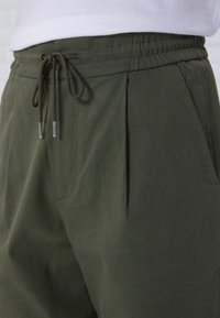 Pantaloni verde oliva con vita elasticizzata, realizzati in tessuto morbido, con pieghe e tasche laterali per una vestibilità comoda.