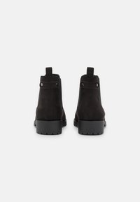 Stivali alla caviglia in suede nero, caratterizzati da una finitura liscia, una robusta suola in gomma, linguetta posteriore e pannelli elastici laterali doppi per un facile indossamento.