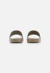 Deux claquettes vues de dos en caoutchouc beige clair avec des lanières incurvées et une semelle texturée. Design simple, semelle plate et sans quincaillerie supplémentaire.