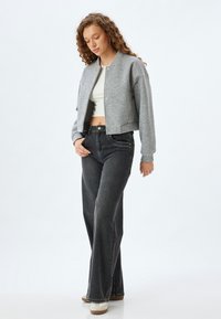 Graues, kurzes Sweatshirt mit Druckknöpfen, kombiniert mit hoch taillierten, dunkelblauen, ausgestellten Jeans und weißen Sneakers. Einfache, weiche Textur.