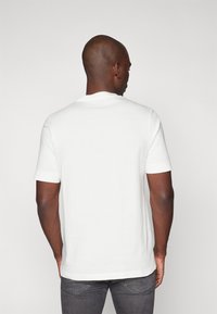 Weißes Kurzarm-T-Shirt aus Baumwolle mit Rundhalsausschnitt und geradem Saum, von hinten vor einem schlichten Hintergrund gezeigt.