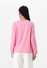 Vaaleanpunainen pitkähihaiset paita, jossa on pystysuorat raidat, pyöreä pääntie ja rento malli. Materiaali näyttää pehmeältä; hihoissa on lievää rypytystä hihansuissa.