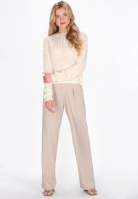 Roomkleurige gebreide trui met een gestructureerd patroon, gecombineerd met beige wijde broekspijpen. Sandalen maken de outfit compleet.