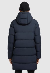 Tumed sinine puffermantel kapuutsiga, millel on tikandmuster, pikad varrukad ja sirge lõige, valmistatud kergest ja soojust säilitavast materjalist.