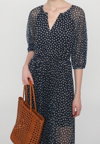 Robe navy à imprimé floral avec des manches bouffantes transparentes et une taille froncée, associée à un sac fourre-tout en orange texturé et tissé.