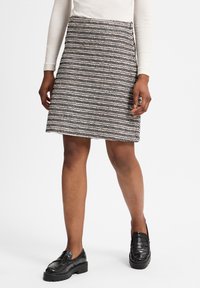 Een knielange rok met een gestructureerd zwart-wit patroon, featuring een aansluitende taille en rechte snit, gecombineerd met zwarte instappers.
