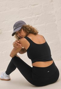 Crna atletska crop majica i tajice s uskim dizajnom; svijetlosiva kapa s "self." logom; glatka tkanina, minimalni detalji.