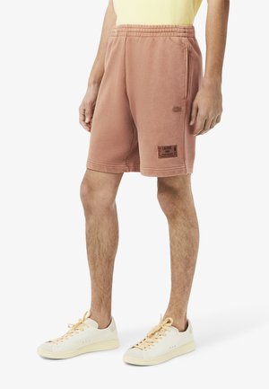 Light brown, cotton blend shorts with an elastic waistband, a patch label on the left thigh, and a small logo embroidered on the side.