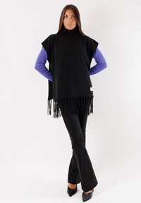 Poncho nero lavorato a maglia con colletto alto, caratterizzato da frange lungo l'orlo. Abbinato a pantaloni neri a zampa d'elefante e tacchi a punta.