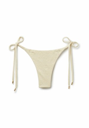 Parte inferior de bikini beige texturizada con lazos laterales y puntas metálicas doradas, colocada plana sobre fondo blanco.