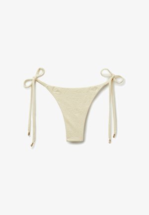 Parte inferior de bikini beige texturizada con lazos laterales y puntas metálicas doradas, colocada plana sobre fondo blanco.