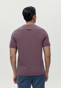 Majica kratkih rukava, boje mauve, pogodna za sport. Glatka textura s crvenim detaljem iznad nazadnog izreza. Ima savremeni dizajn.