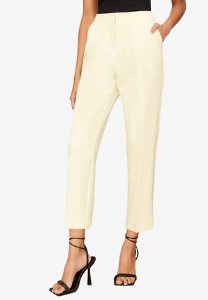 Pantaloni dritti color crema con tasche laterali, una superficie liscia e una vita a media altezza. Abbinati a sandali neri con cinturini e tacco alto.