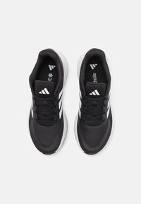 Černé sportovní boty s bílými pruhy, síťovaným svrškem, polstrovanou podrážkou a tradičním zavazováním na tkaničky. Po bocích mají texturované detaily.