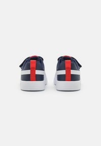 Chaussures de sport bleu marine et blanches avec des accents rouges, dotées d'un dessous texturé, d'un contre-fort de talon renforcé et d'une lanière pour un enfilage facile.