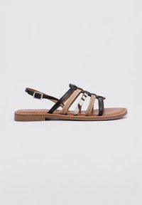 Sandalia plana negra y marrón con tiras, que presenta múltiples correas de diversas texturas y colores, aseguradas por una correa en el tobillo con hebilla.